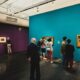 Visitors viewing paintings in a gallery with turquoise and purple walls in São Paulo
