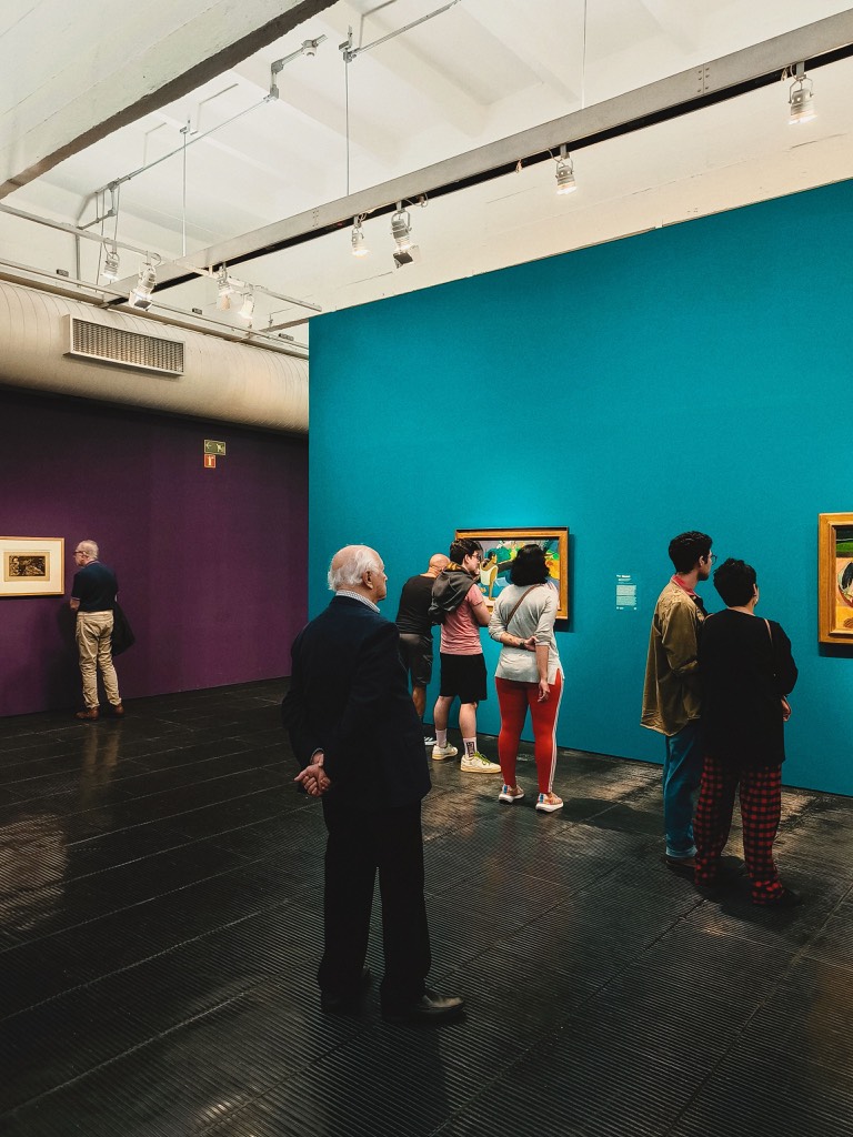 Visitors viewing paintings in a gallery with turquoise and purple walls in São Paulo