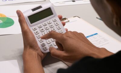 Hands using a white calculator beside printed charts and financial documents