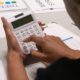 Hands using a white calculator beside printed charts and financial documents