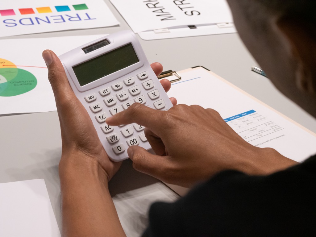 Hands using a white calculator beside printed charts and financial documents