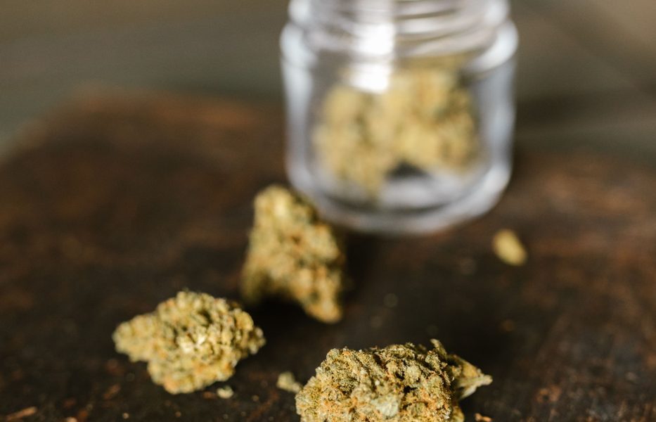 Dried cannabis flowers beside a glass jar
