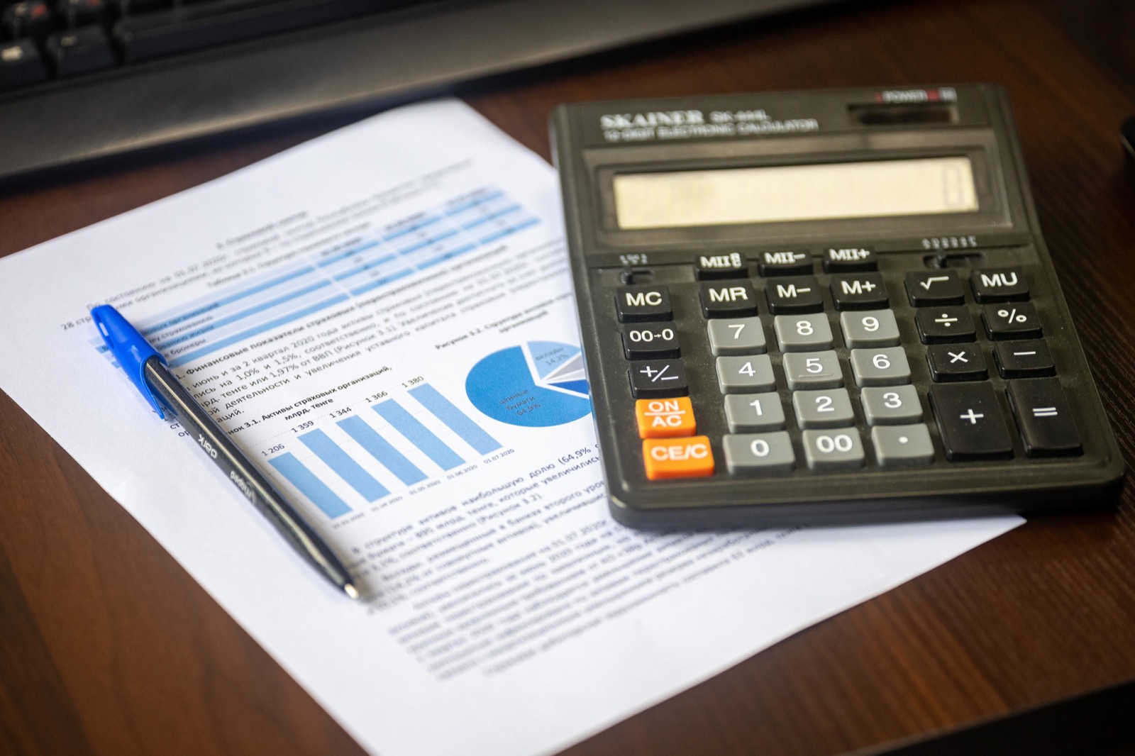 A calculator and blue pen resting on a printed financial report