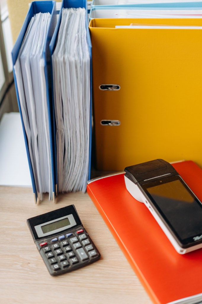 Calculator and payment terminal beside upright office binders