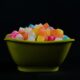 Colorful gummy candies in a green bowl against a dark background