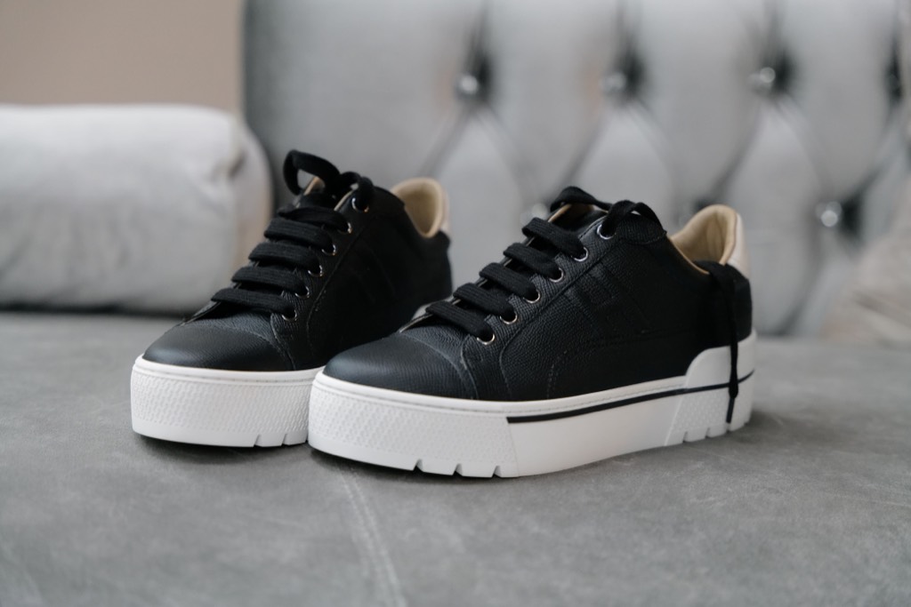 Black leather sneakers with white soles on a gray upholstered seat