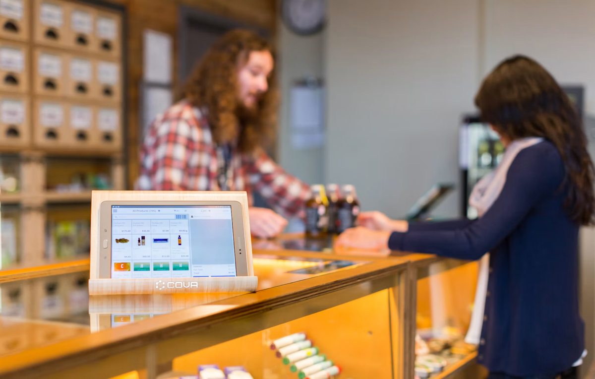 Point-of-sale screen on a cannabis dispensary counter with people in the background