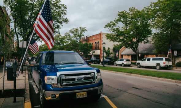 Small-town main street with American flags and parked vehicles