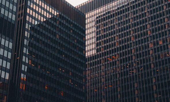 Glass office buildings viewed from below against a pale sky