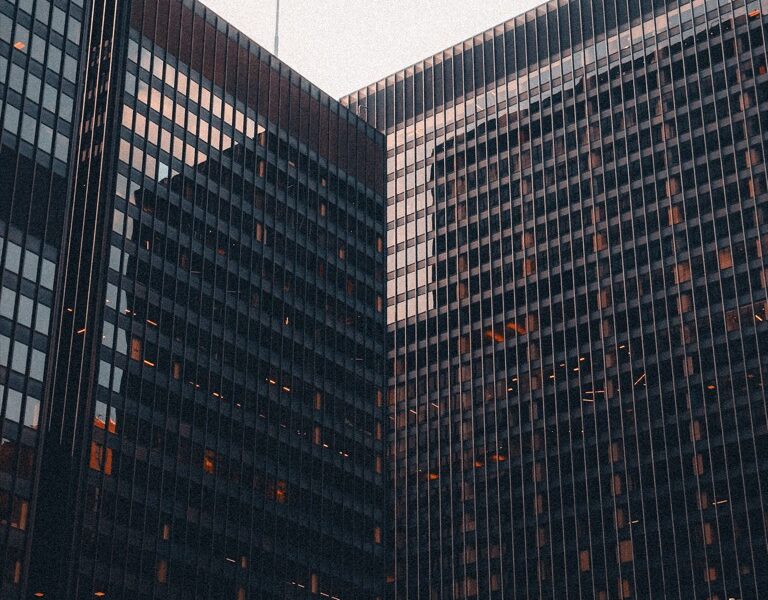 Glass office buildings viewed from below against a pale sky