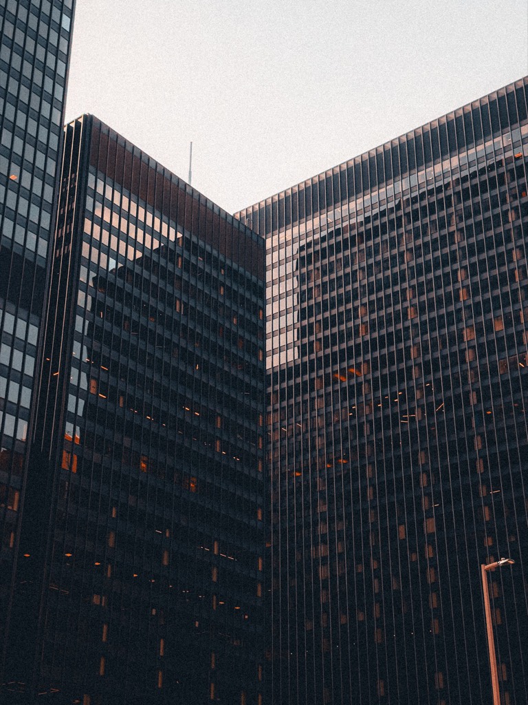 Glass office buildings viewed from below against a pale sky
