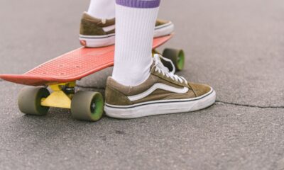 Olive sneakers and white striped socks beside a red skateboard on pavement