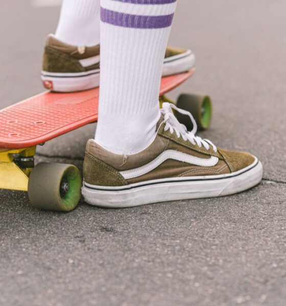 Olive sneakers and white striped socks beside a red skateboard on pavement