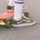 Olive sneakers and white striped socks beside a red skateboard on pavement