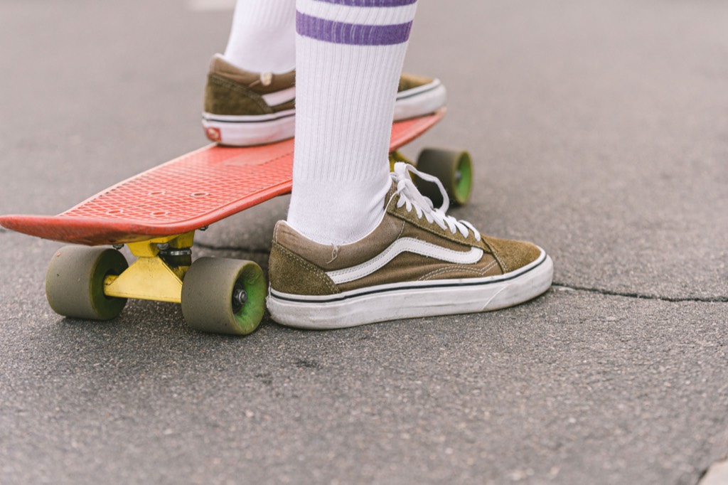 Olive sneakers and white striped socks beside a red skateboard on pavement